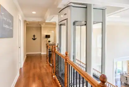 A Stiltz residential elevator installed in a hallway next to a wooden staircase.