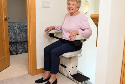 A woman sits on a stairlift positioned at the top of a staircase.